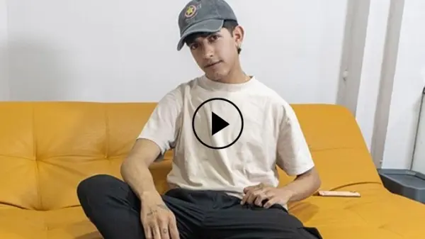 Teo LatinBoyz model sitting on couch with video play button overlay for trailer preview