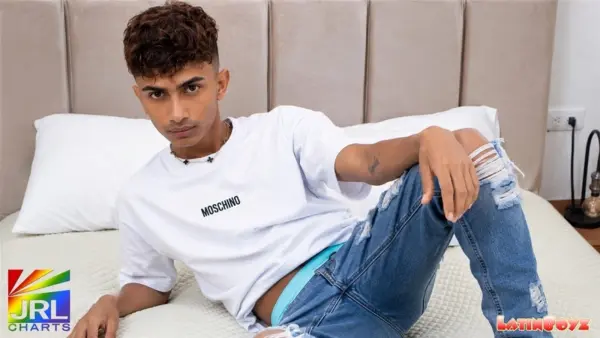 Peter of LatinBoyz reclines on a bed in a casual bedroom portrait image featured on JRL CHARTS Gay News.